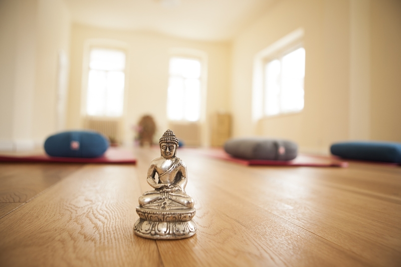eine Buddha Statue steht im Yogaraum im Vordergrund, mystische Atmosphäre, hell