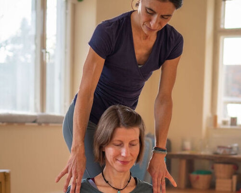 Claudia unterstützt Sonja sanft an den Schultern, im Yoga