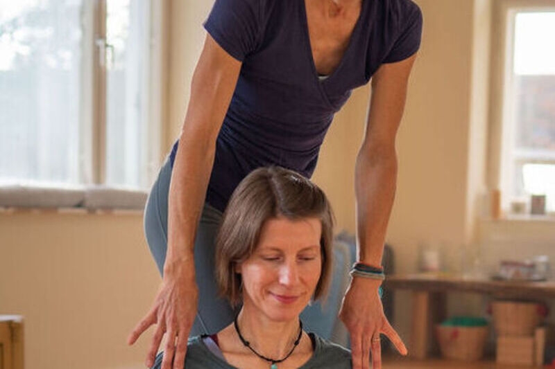 Claudia unterstützt Sonja sanft an den Schultern, im Yoga